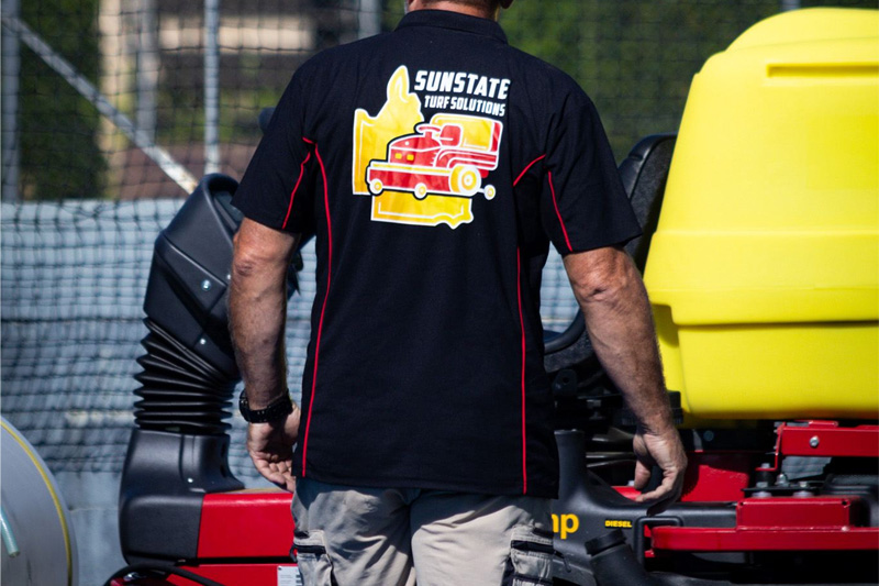 Operator in a branded work shirt standing beside the turf cleaning machine
