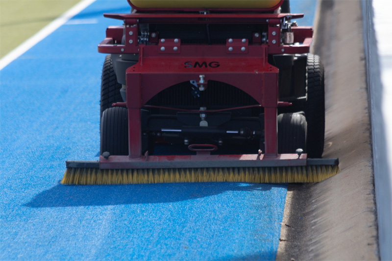 Wide brush on the turf machine sweeping blue synthetic turf along a kerb