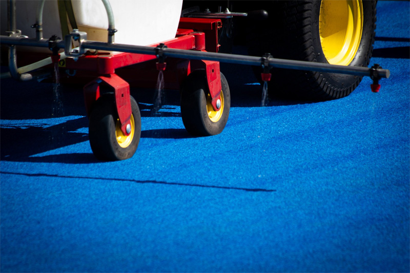 Close-up of a spray boom dripping cleaning solution onto blue synthetic turf