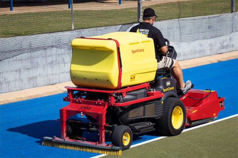 Turf cleaning machine with a front brush working across a blue hockey field