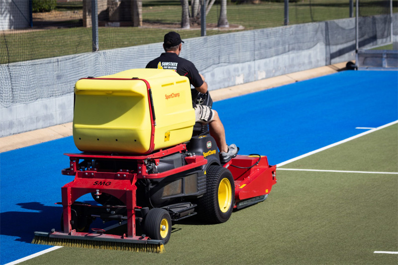 Turf cleaning machine driving away down the blue run-off area of a hockey field