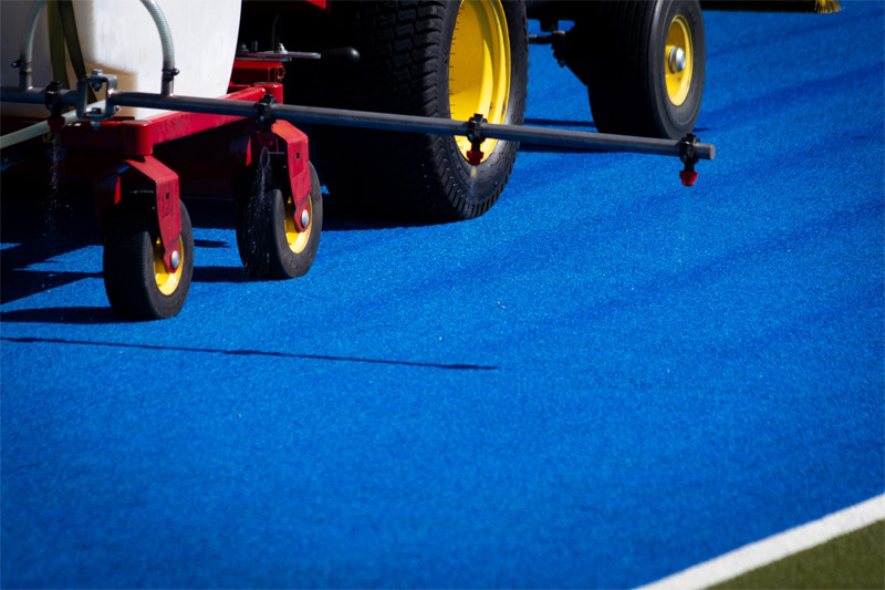 Spray boom and yellow trailer wheels on blue synthetic turf